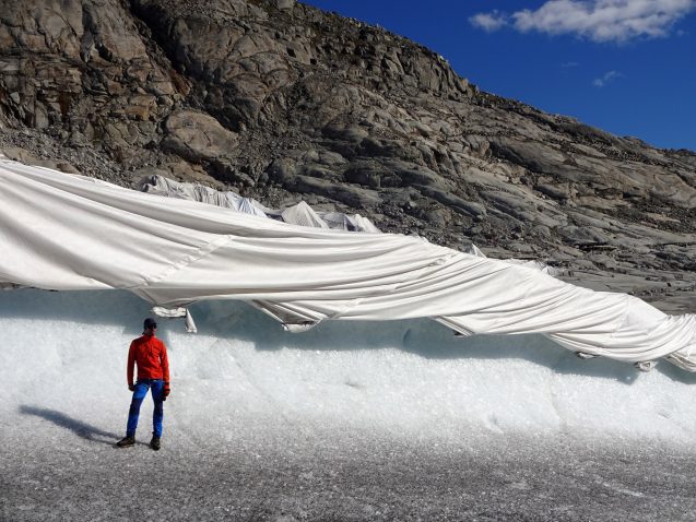 一名研究人员站在罗纳冰川前，覆盖着土工布，以防止冰川加速融化。©Matthias Huss
